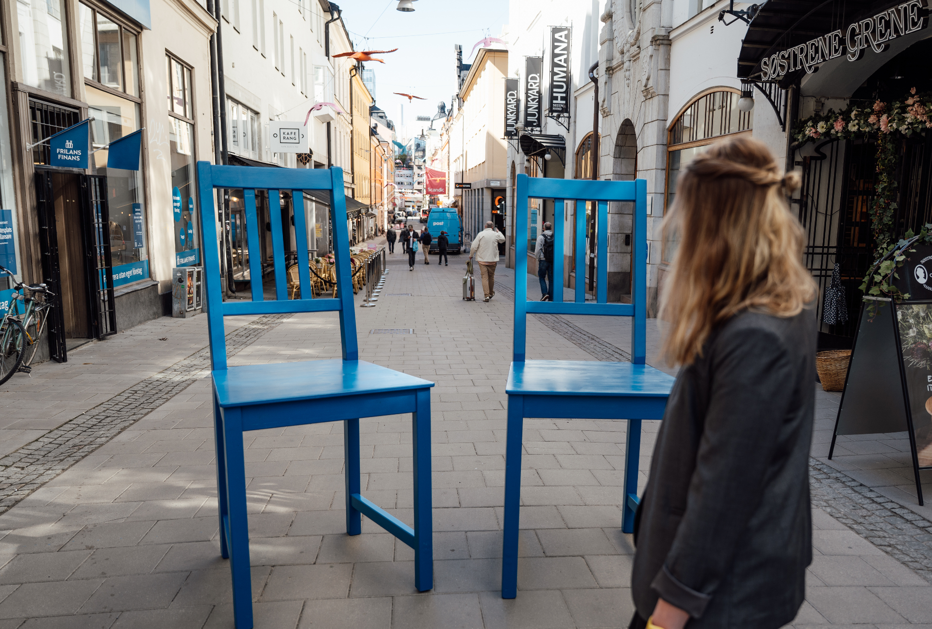 Två stora blå stolar uppställda på en gågata i Stockholm, med en kvinna som betraktar dem.